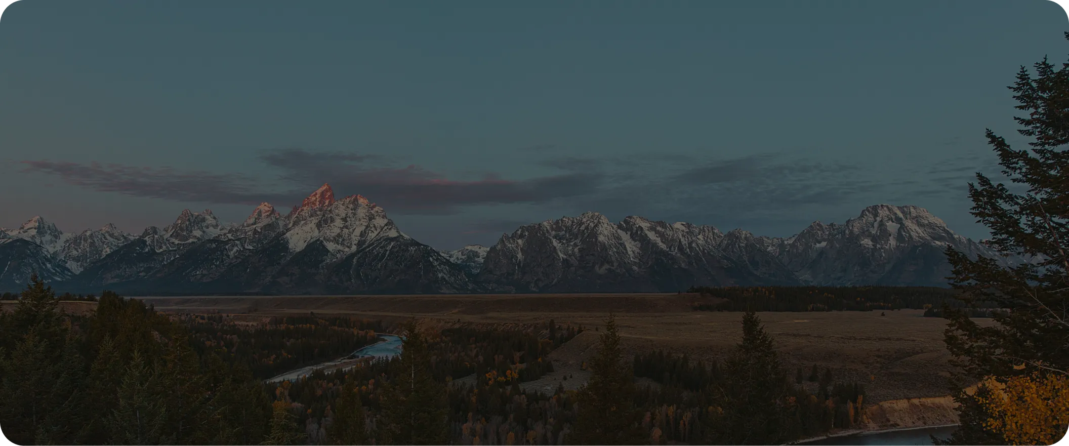 Panoramic view of the Teton mountain range at sunset with a river valley in the foreground