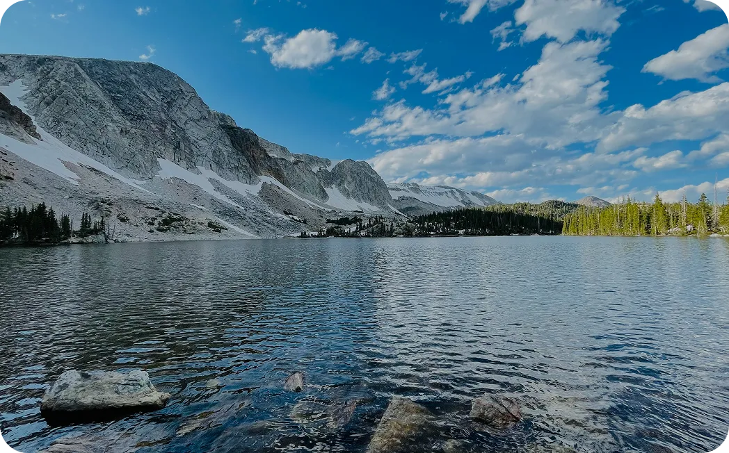 Clear mountain lake reflecting blue sky and rugged peaks surrounded by evergreen trees