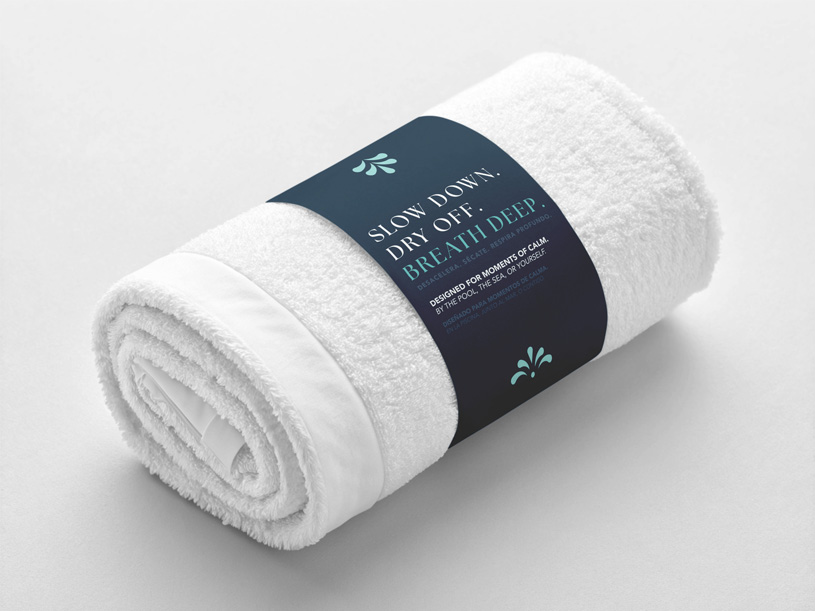 Rolled white towel with a dark blue label reading 'Slow down. Dry off. Breathe deep.' on a light surface.