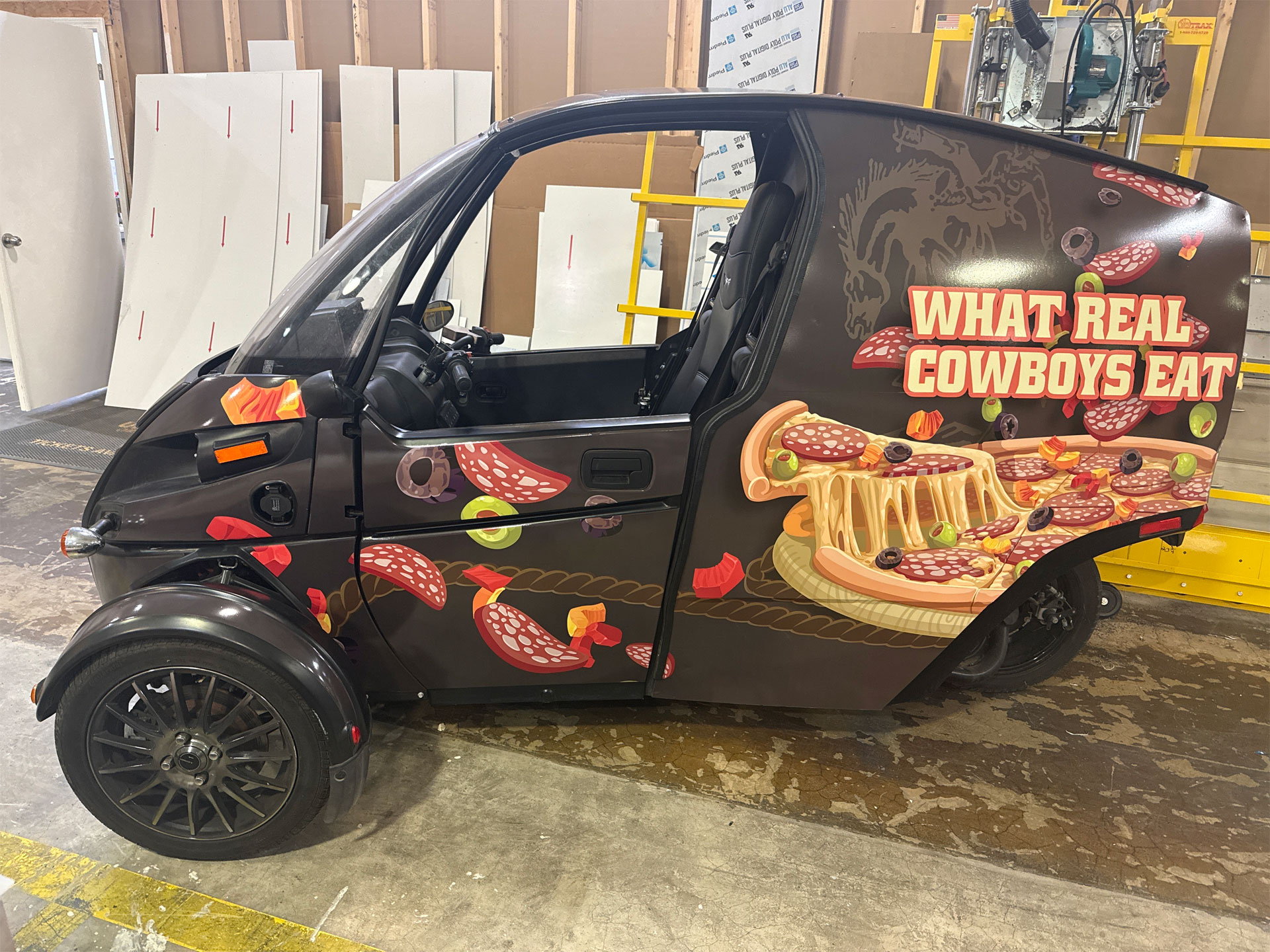 Small three-wheeled black vehicle with pizza-themed wrap and text reading 'WHAT REAL COWBOYS EAT' on the side.