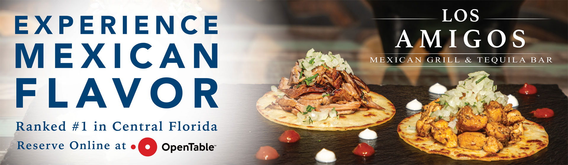 Two tacos topped with chopped onions and cilantro on a dark surface with sauce dots, alongside text promoting Los Amigos Mexican Grill & Tequila Bar.