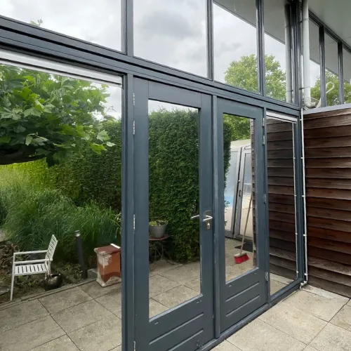 Glazen terrasdeuren met zonwerende folie met zwarte kozijnen die doen denken aan een tuin met groen en tuinmeubilair.