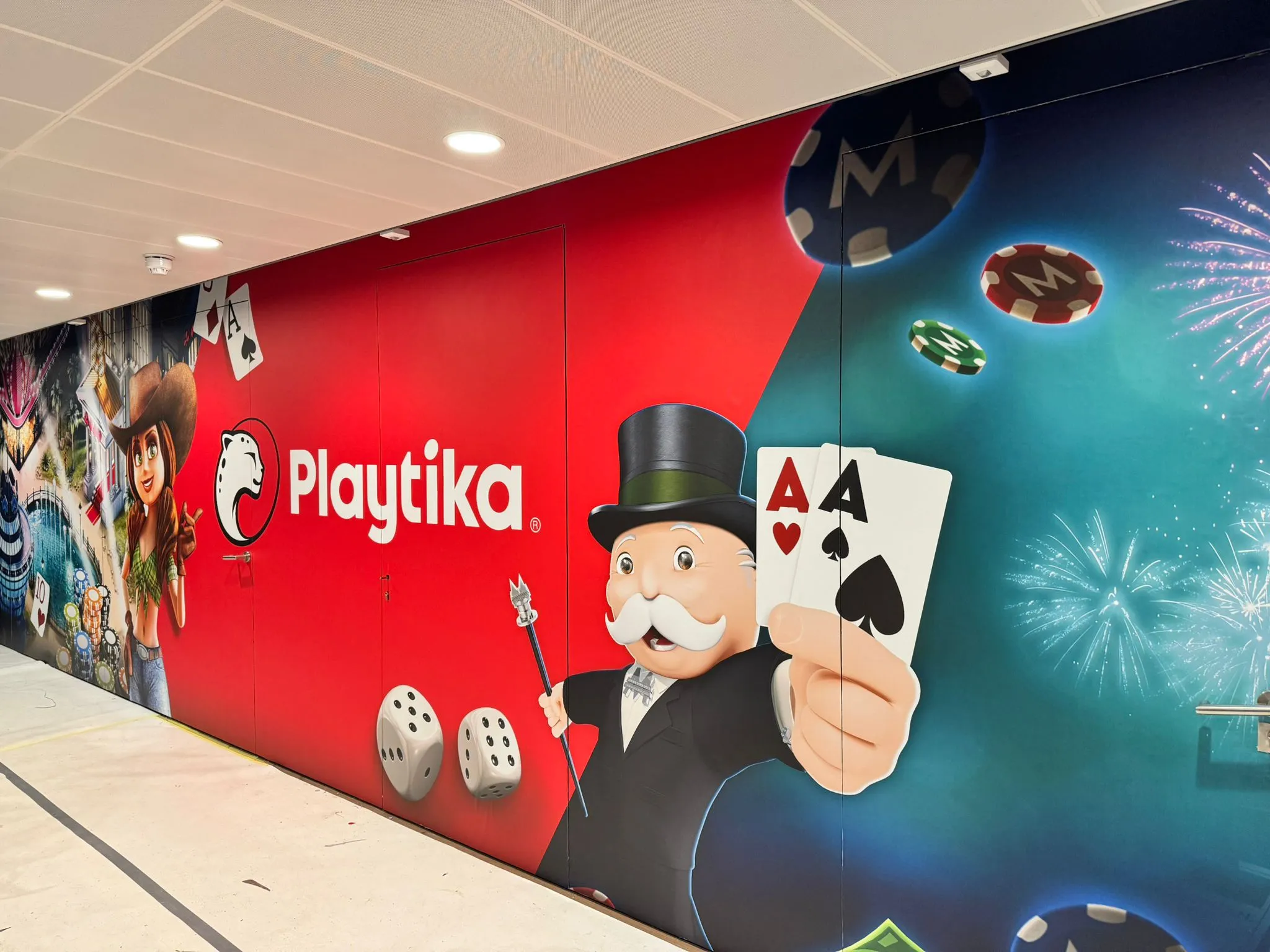 Muurprint met het Playtika-logo, geanimeerde personages, dobbelstenen, pokerchips, speelkaarten met azen en vuurwerk.