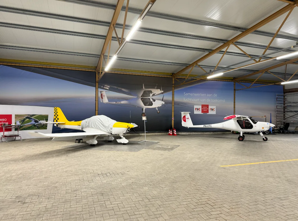 Twee kleine vliegtuigen geparkeerd in een hangar met luchtvaartmuurschilderingen op de wanden.
