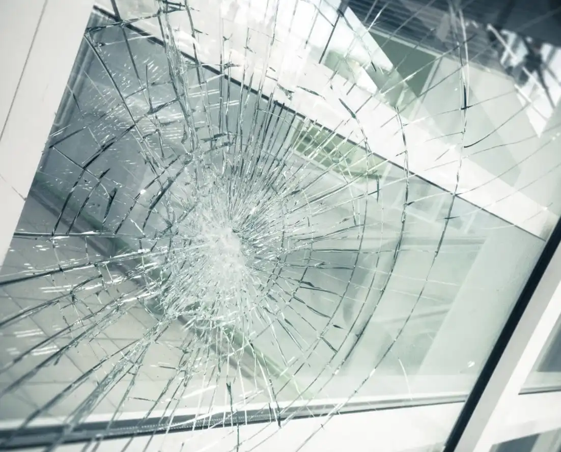 Close-up van een gebarsten en verbrijzeld glasraam met een cirkelvormig inslagpatroon.