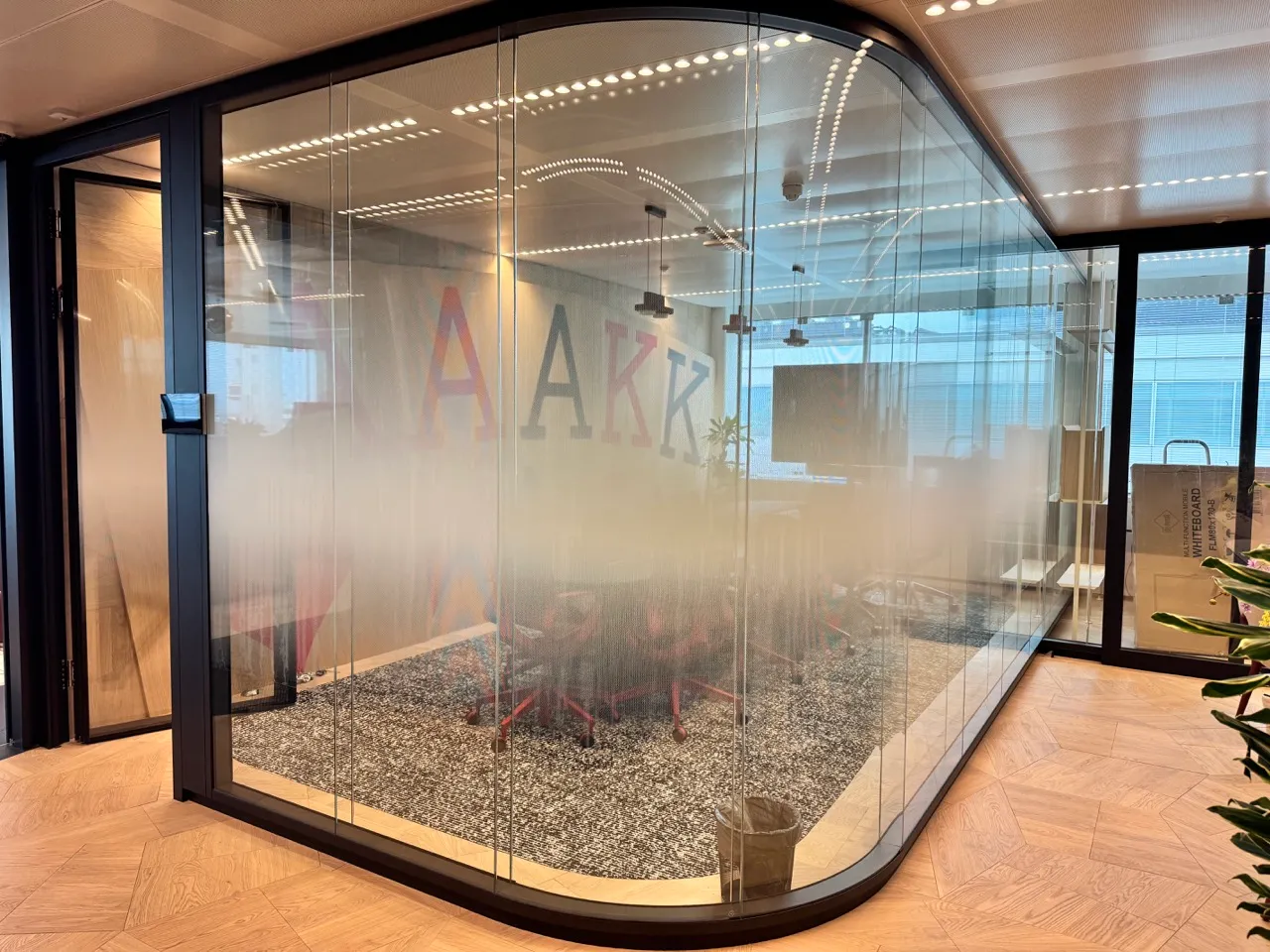 Moderne vergaderruimte in een kantoor, omsloten door glazen wanden met een matte middenstrook, voorzien van stoelen en tapijt.