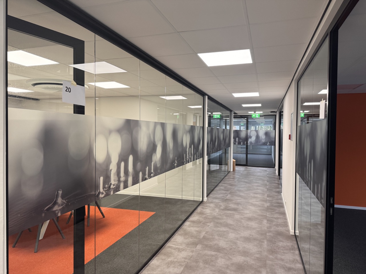 Moderne kantoorgang met glazen wanden, matte folie en een oranje tapijt in de vergaderruimte.