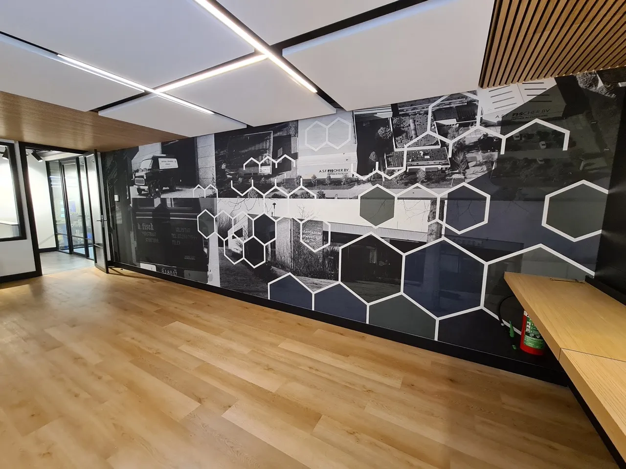 Minimalistische kantoorruimte met houten vloer, een zwart-witte geometrische muurschildering en plafondverlichting.