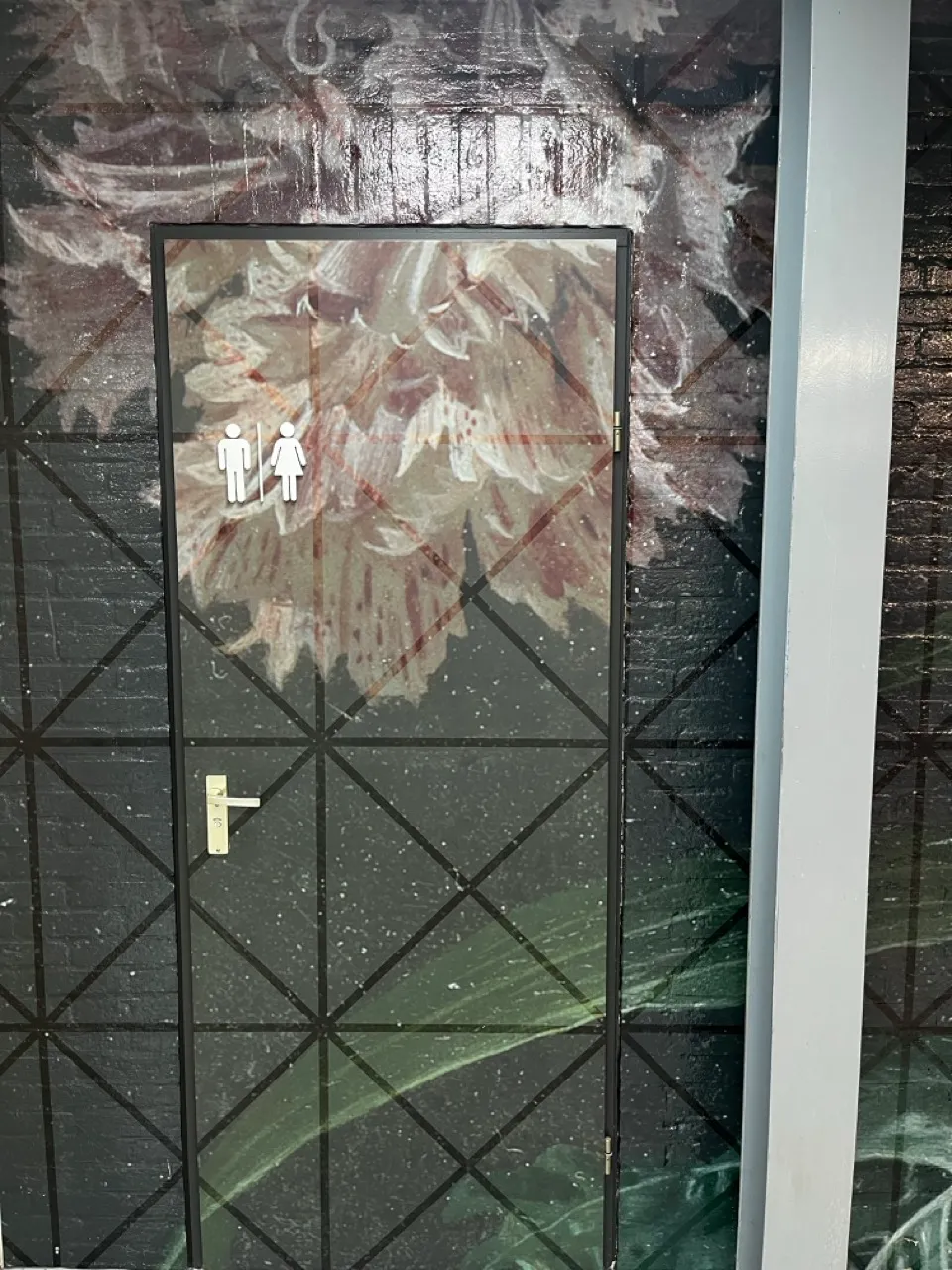 Deur beschilderd met een grote bloemenmuurschildering met roze bloemen en groene bladeren, met man- en vrouwentoilet-symbolen linksboven.