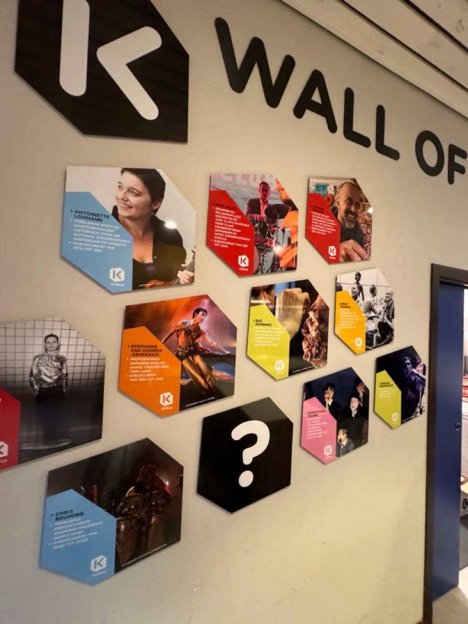 Wall of Fame met hexagonale plaquettes met portretten en beschrijvingen van bekende personen, waaronder muzikanten en artiesten.