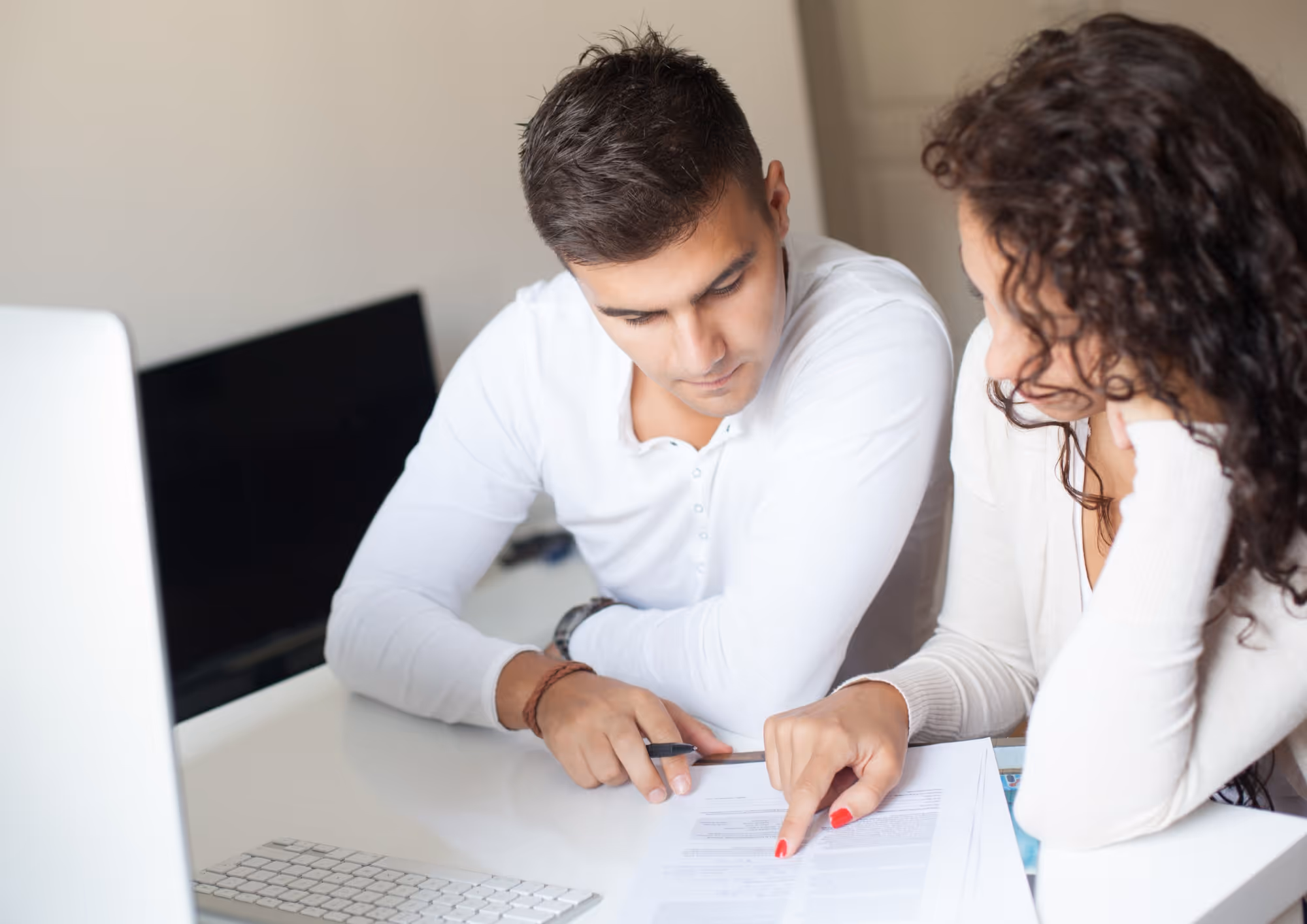 Man and woman reviewing a document together at a desk with a computer keyboard and monitor.