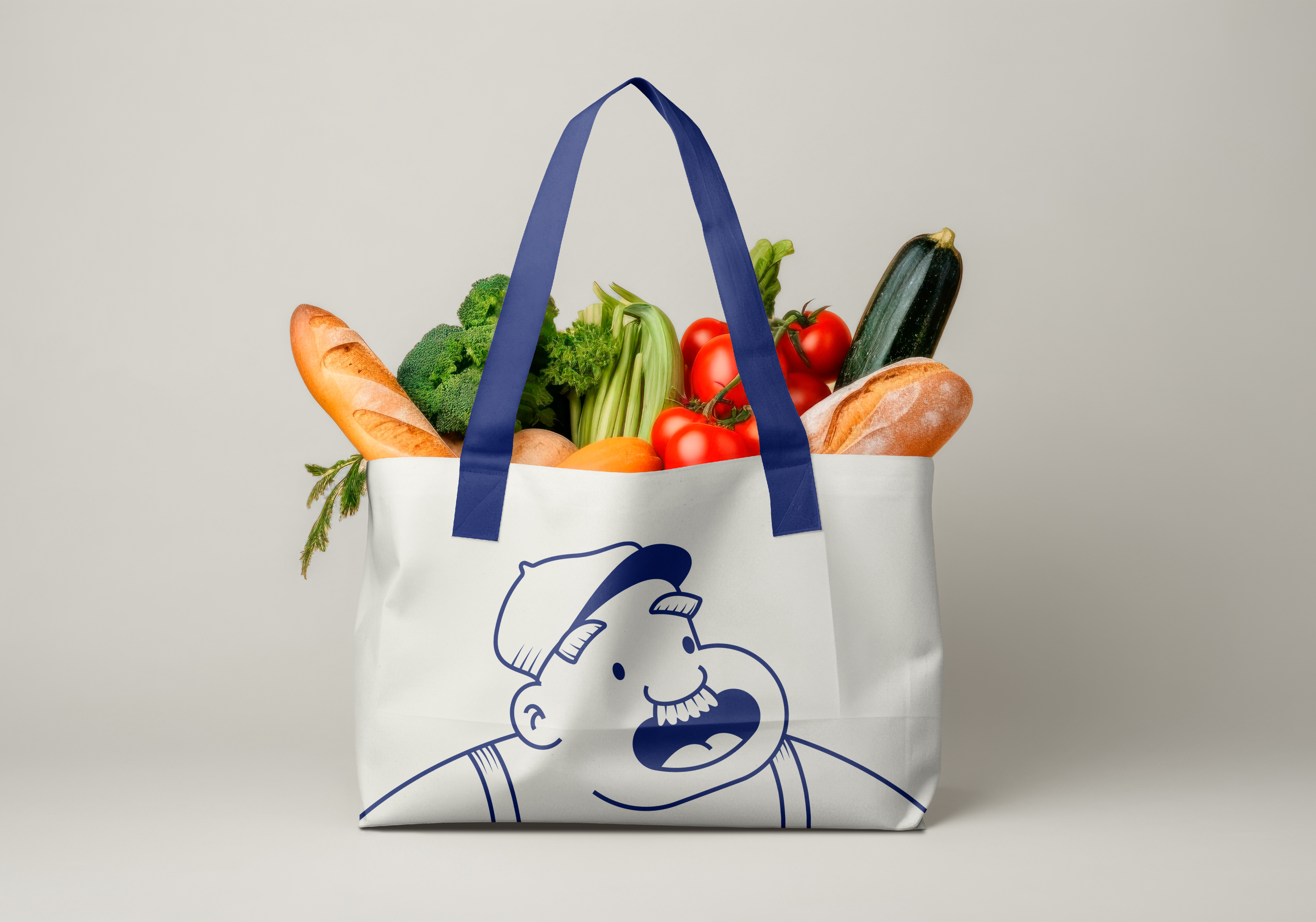 White reusable shopping bag with navy blue handles and a cartoon man illustration, filled with fresh vegetables and baguettes.