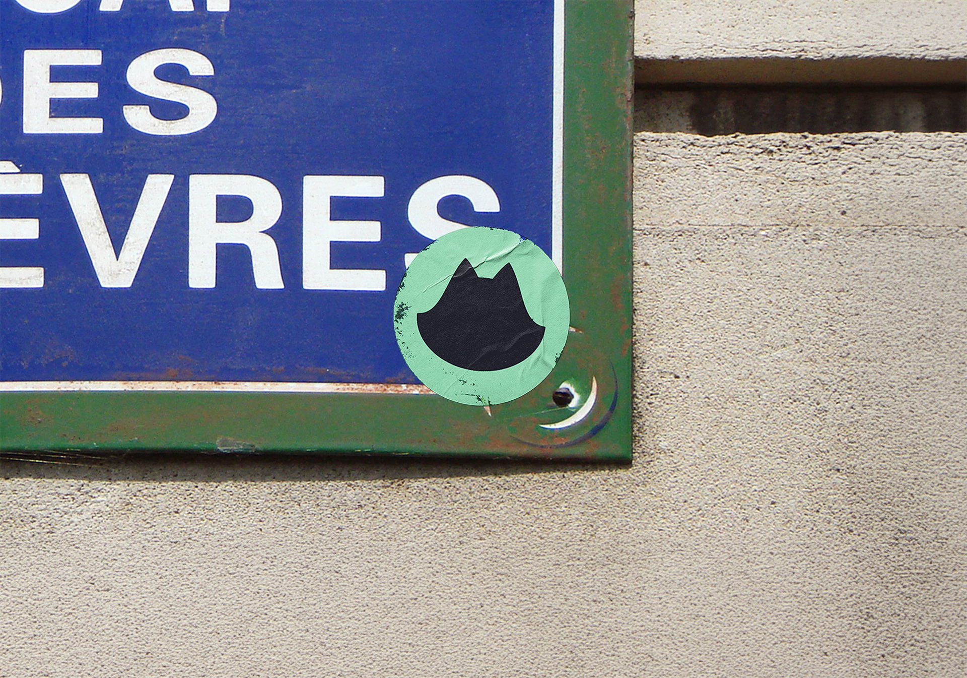 Coin inférieur droit d'un panneau bleu avec cadre vert fixé à un mur beige, affichant un autocollant rond vert avec silhouette noire de chat.