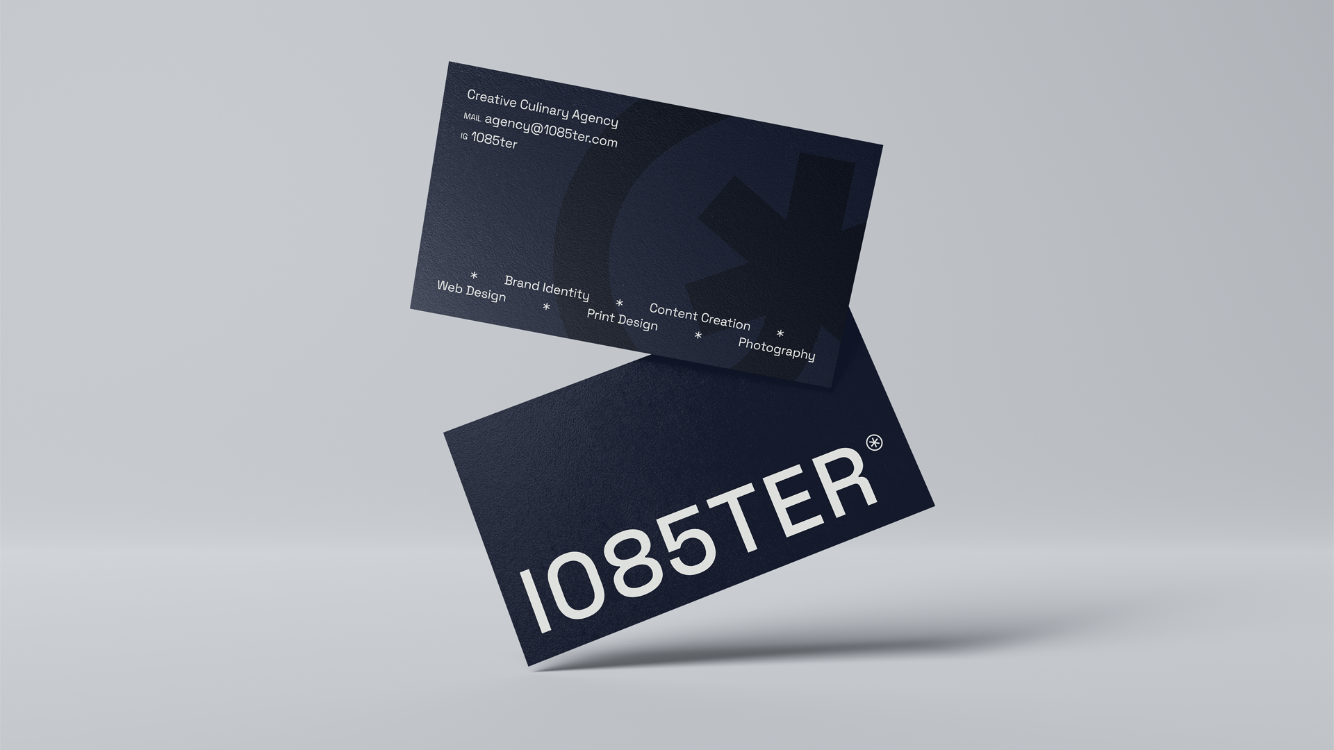 Deux cartes de visite noires en suspension, une affichant le texte '1085TER' et l'autre présentant les services d'une agence culinaire créative incluant design web, identité de marque, design imprimé, création de contenu et photographie.