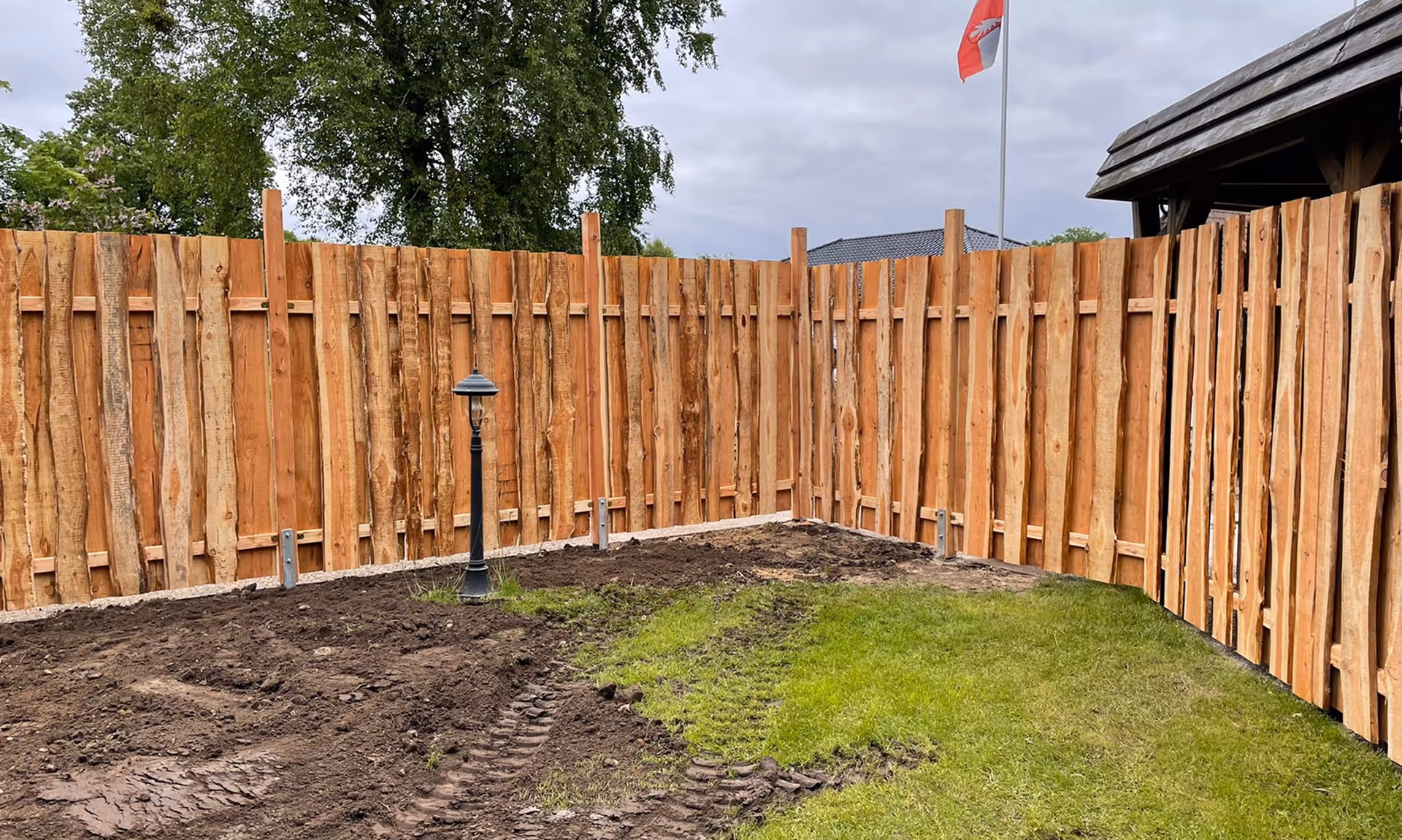 Garten mit einem neuen Holzzaun, teilweise umgebrochener Bodenfläche.
