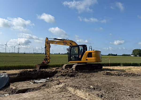 Gelber Bagger gräbt in einem Feld vor blauem Himmel.