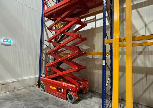 Roter Scherenarbeitsbühne im ausgestellten Zustand in einem Lager.