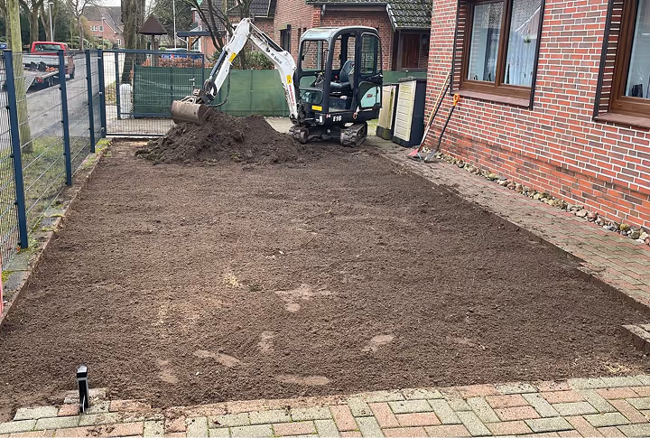 Kleiner Bagger hebt Erde in einem Vorgarten aus neben einem Haus.