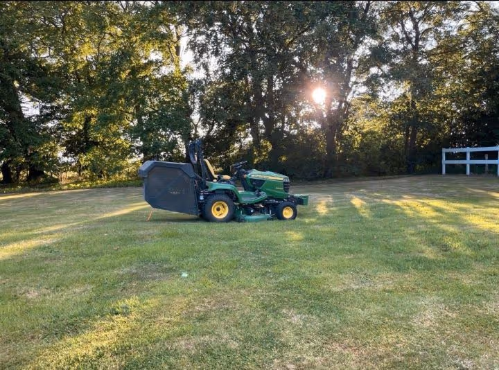 Grüner Rasenmäher auf einer großen, gepflegten Rasenfläche.