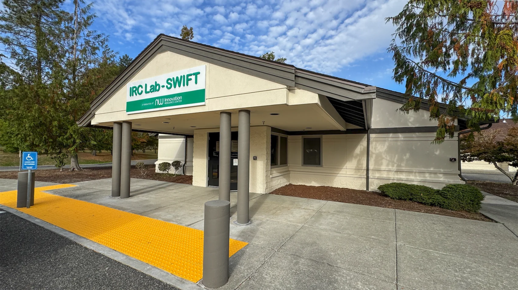 Light stucco building with dark trim, columned covered entry with signage in the gable.