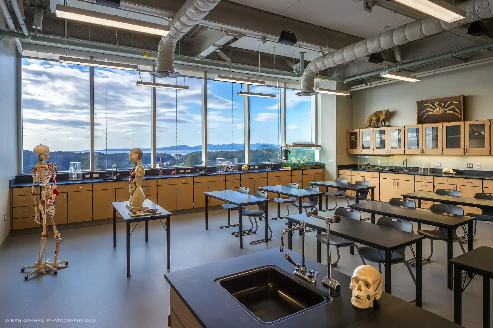 Interior of a school science lab with wood cabinets, black work tables, and a wall of windows overlooking the ocean.