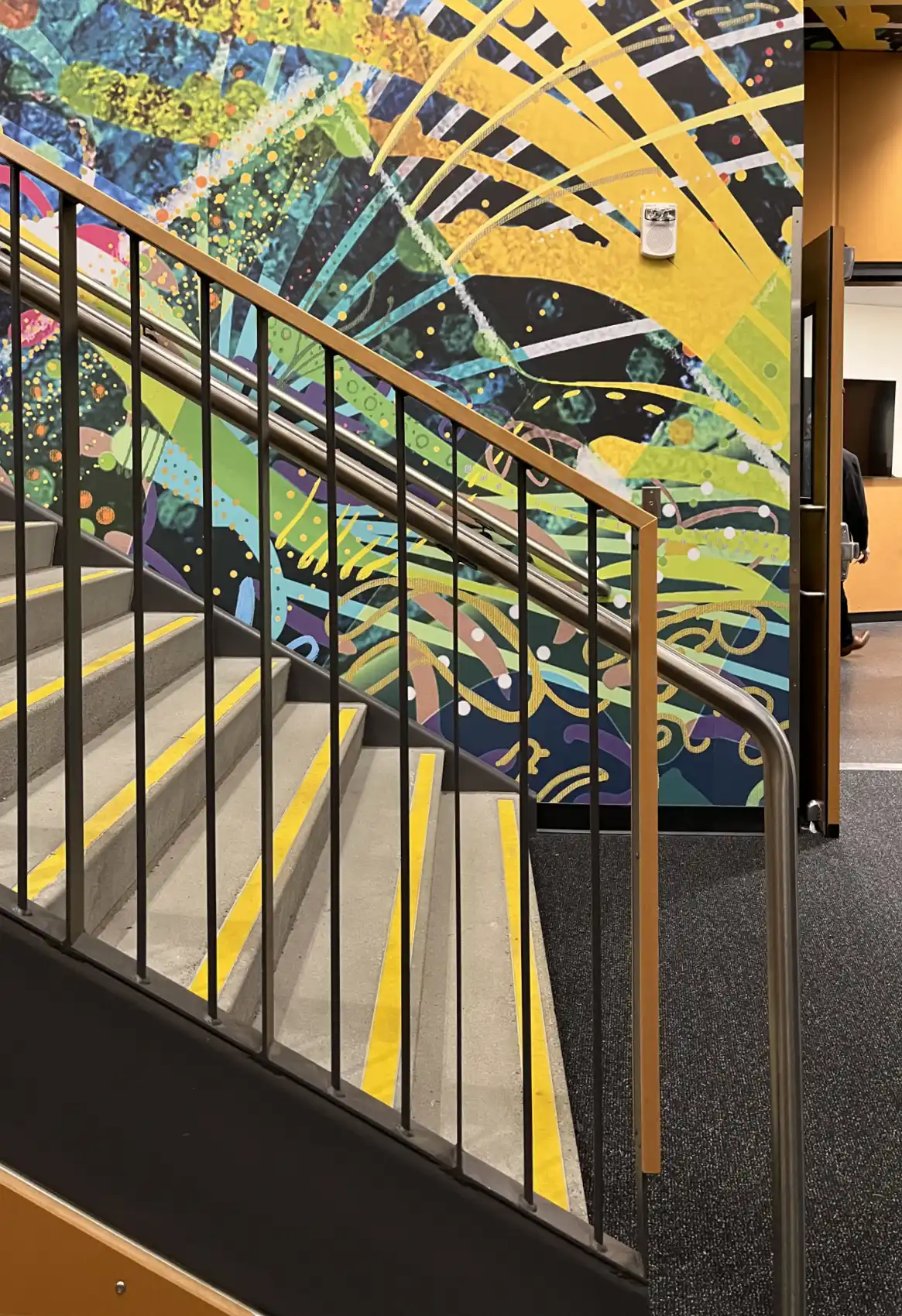 Brightly colored abstract mural behind concrete, metal, and wood stairs.