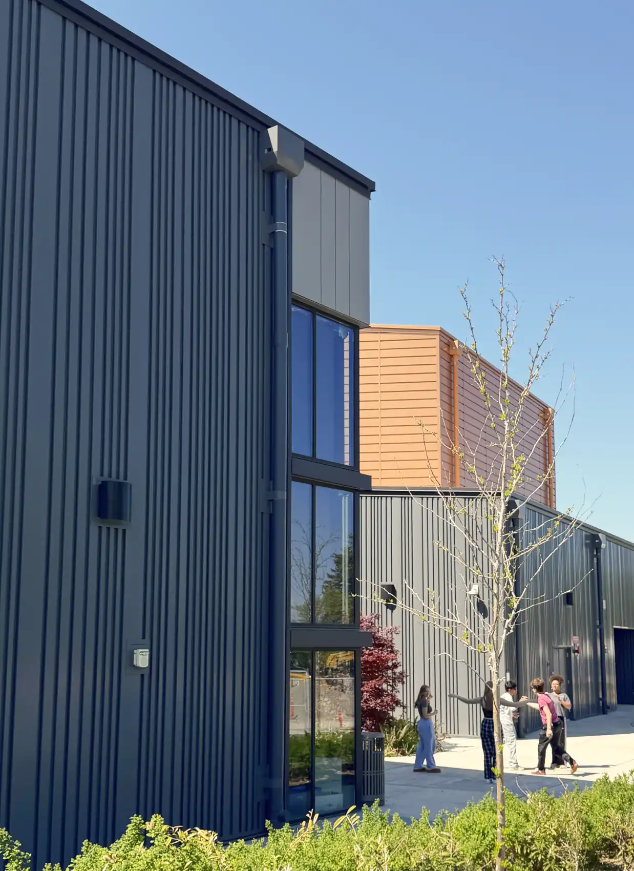 Layered photo the exterior classrooms with metal siding and the copper clad hall behind.