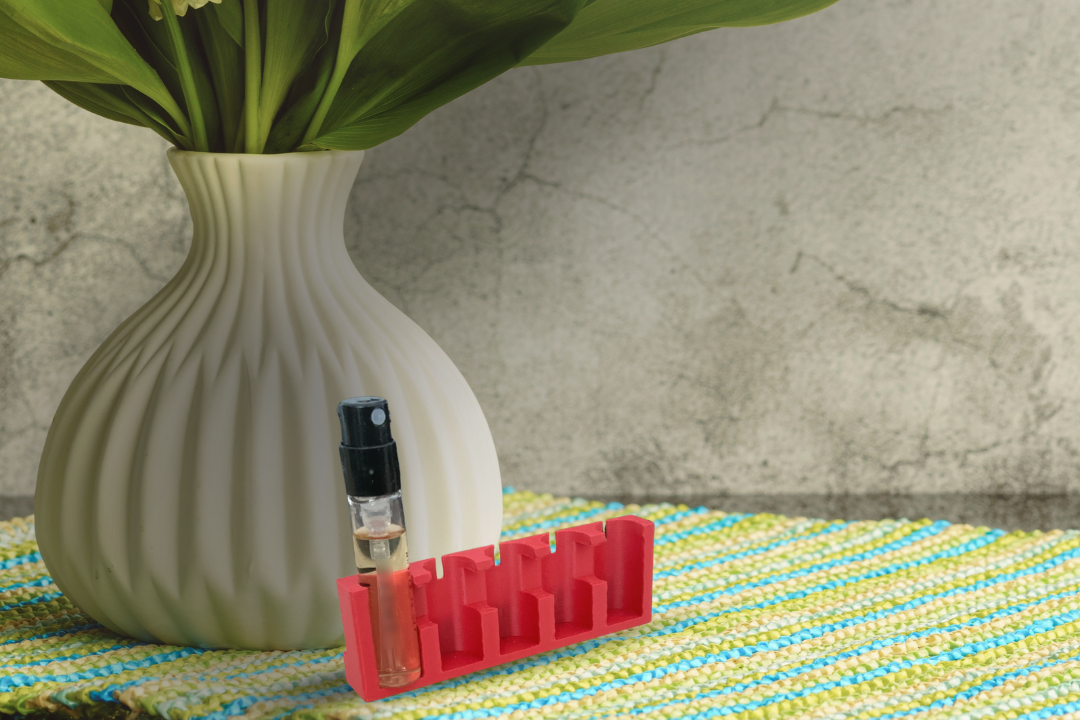 Set de parfumerie avec 10 petits échantillons, un coffret rouge "Nosebook" ouvert avec un stylo, une touche rouge et une tasse blanche sur une table noire.