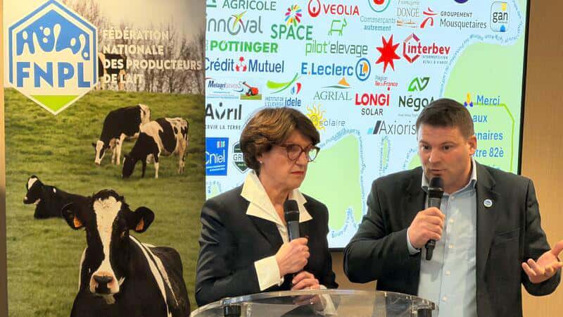 Two people speaking at a podium with microphones in front of a screen showing a map with various company logos, and a banner with cows and FNPL logo behind them.
