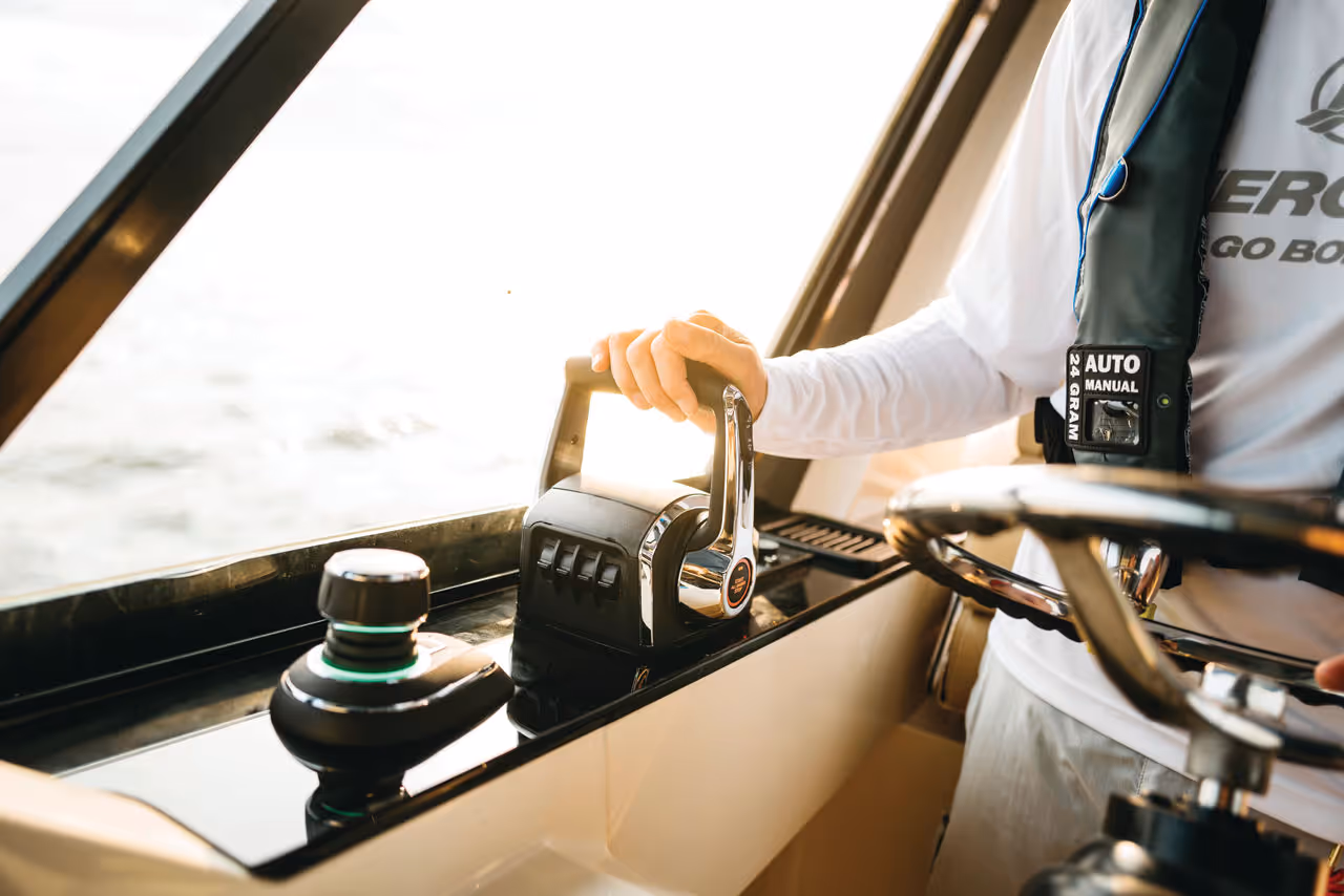 Person steering a boat using throttle controls and a steering wheel inside the cabin.