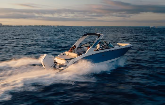 White and blue motorboat speeding on ocean water during sunset with two passengers onboard.