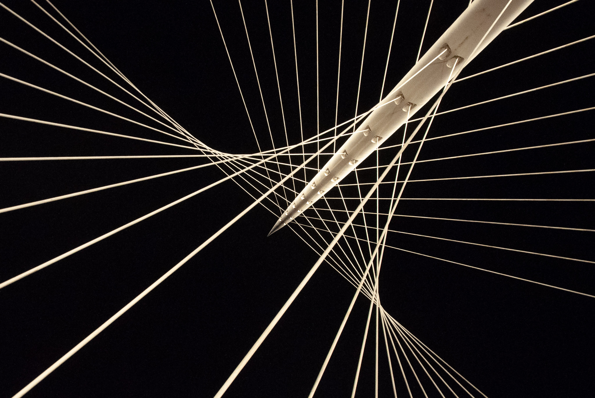 Close-up underside view of a modern cable-stayed bridge with white cables radiating from a central pylon against a dark sky.