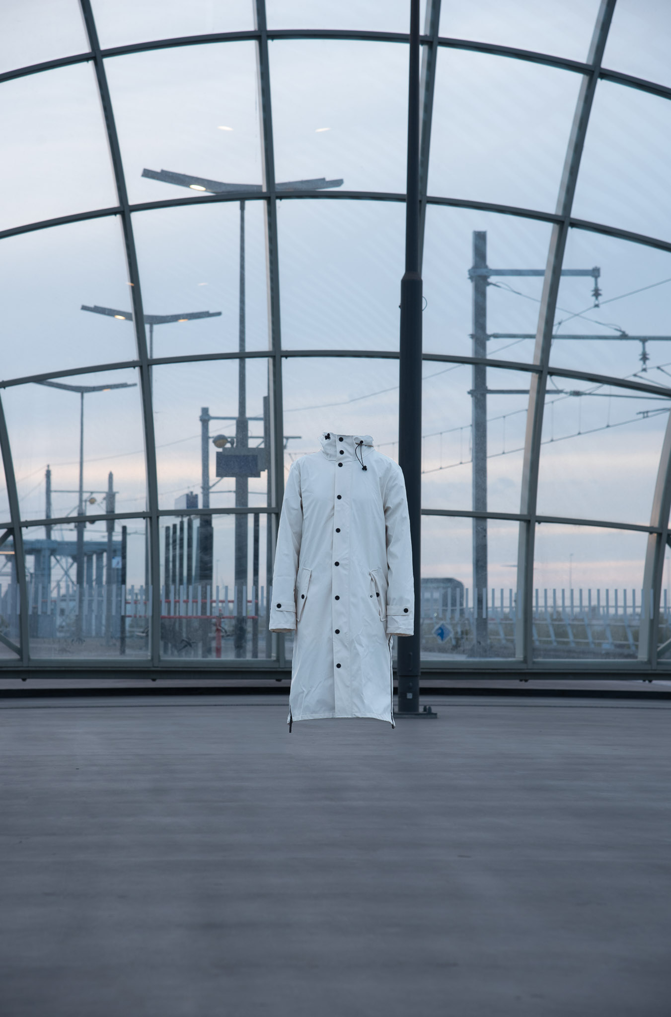 Light-colored long coat floating headless in a large modern glass and metal structure.