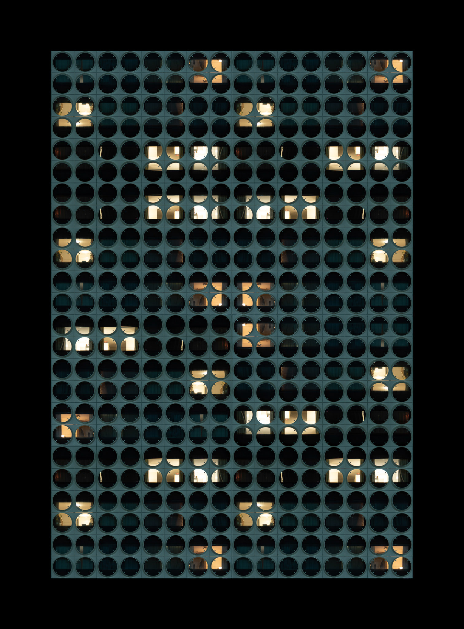 Facade of a building with round windows, some illuminated showing interior rooms with warm light.