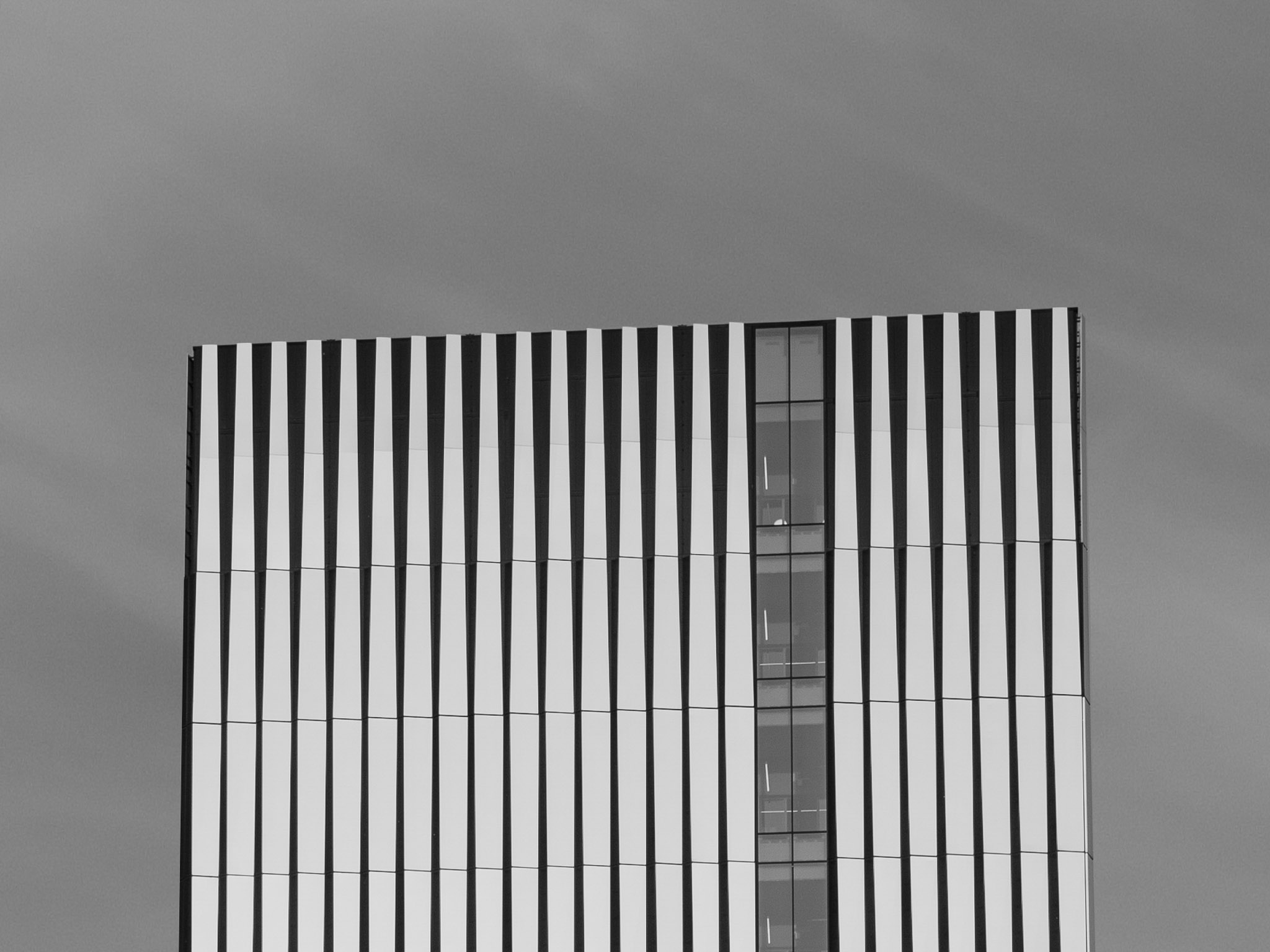 Upper section of a modern building with vertical black and white striped patterns and a central glass window column.