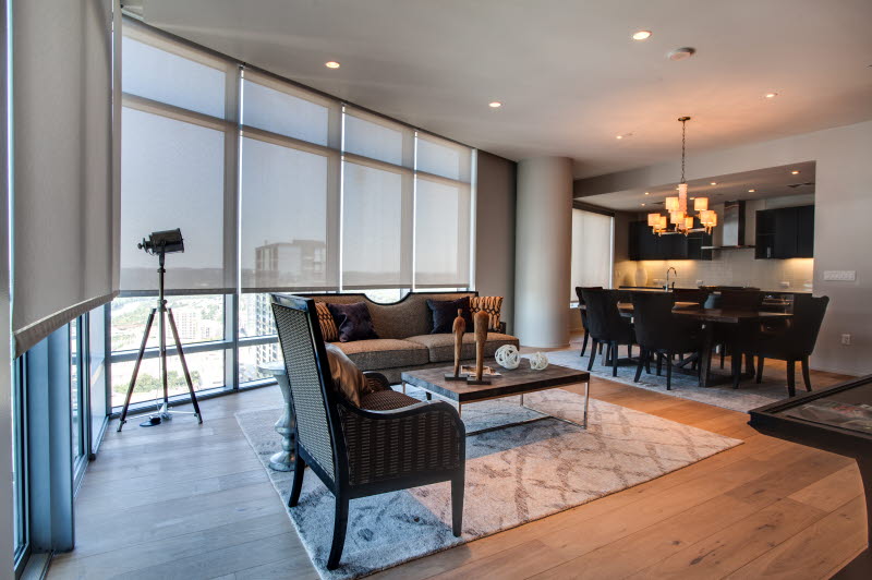 Modern apartment living and dining area with floor-to-ceiling windows and roller shades providing light control and privacy.