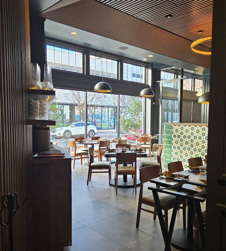Restaurant dining space with large storefront windows, pendant lighting, and interior shading that filters daylight while maintaining an open atmosphere.
