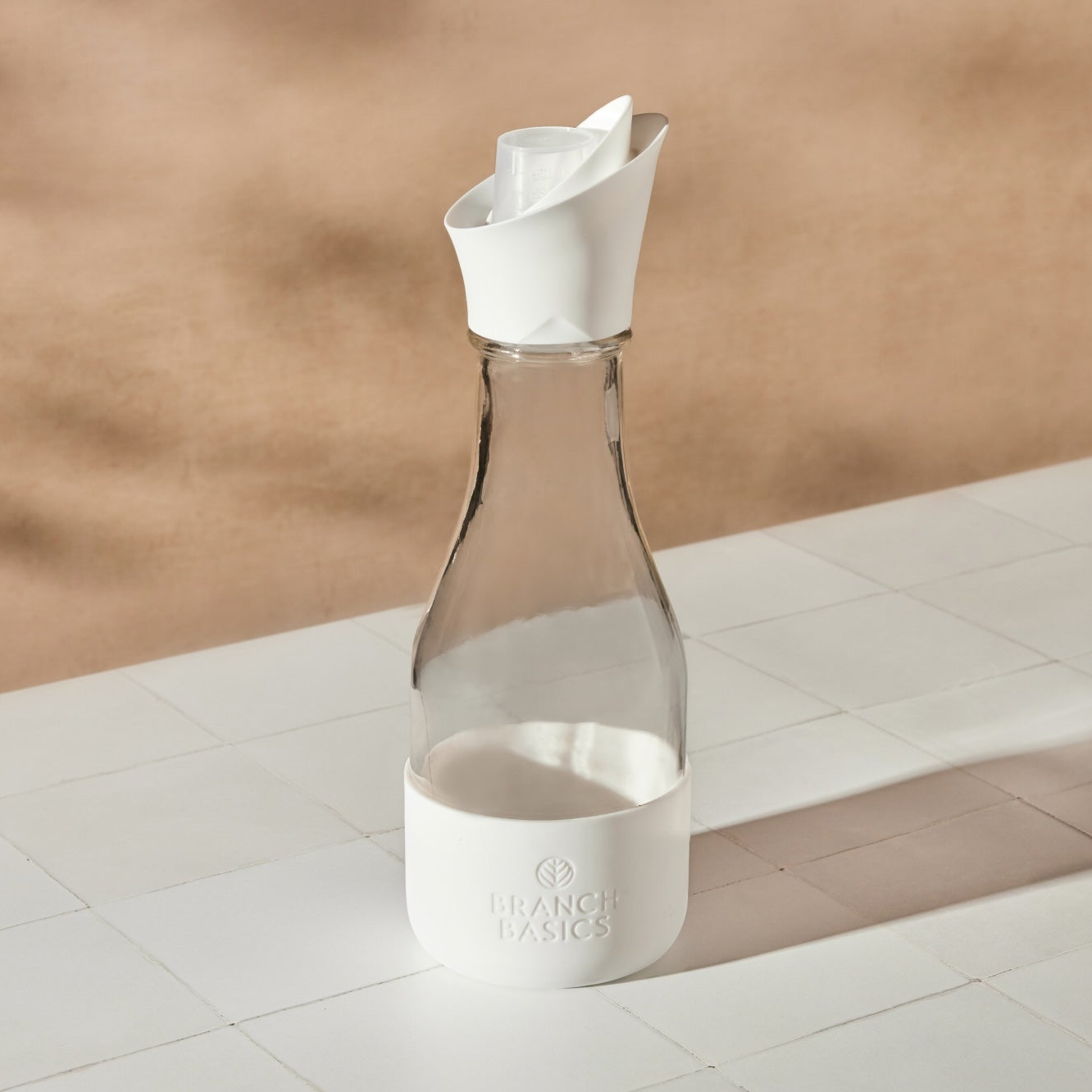 Clear glass Branch Basics carafe with a white sleeve and folded paper top on a tiled surface