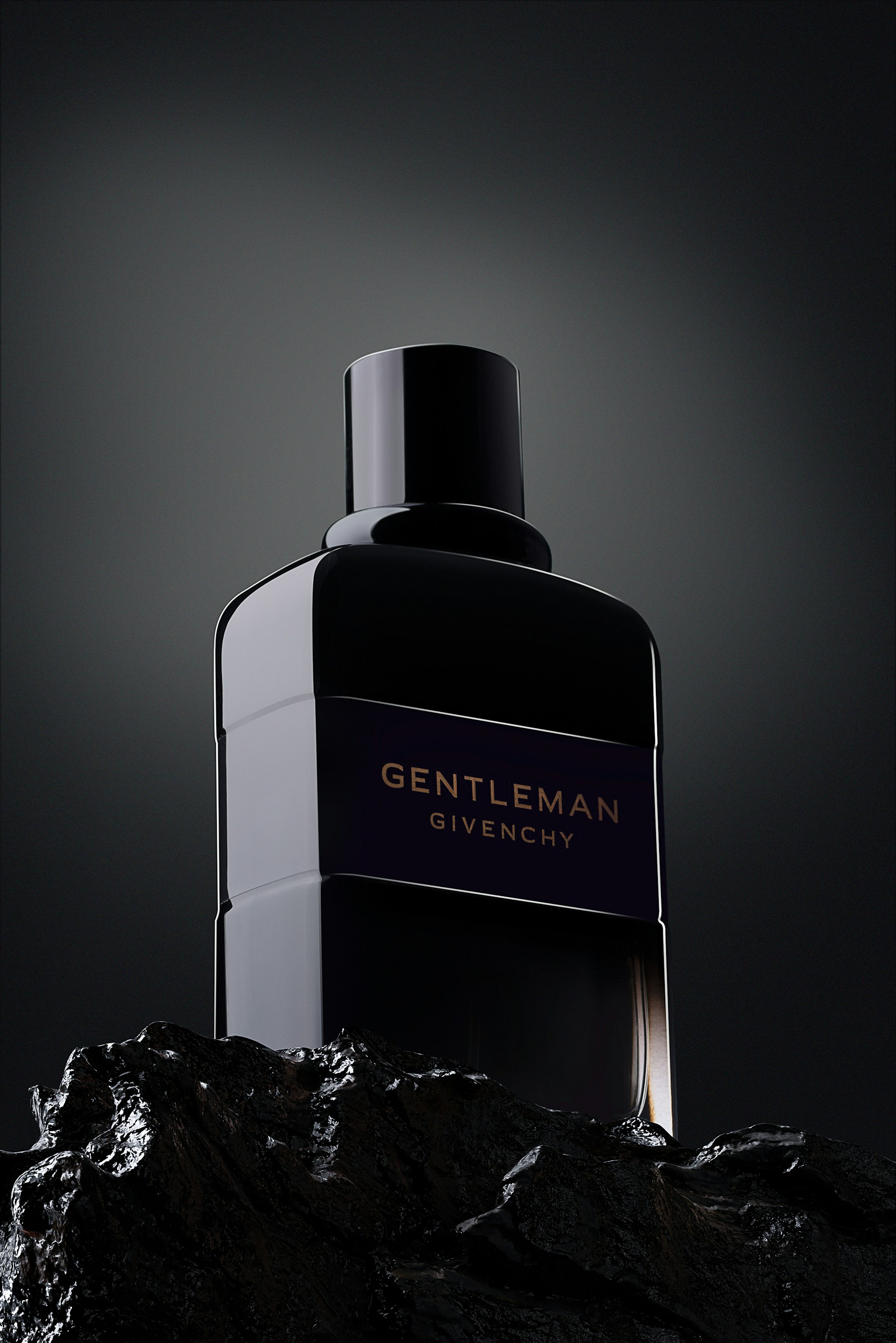 A dark navy fragrance bottle standing on black rock in low light
