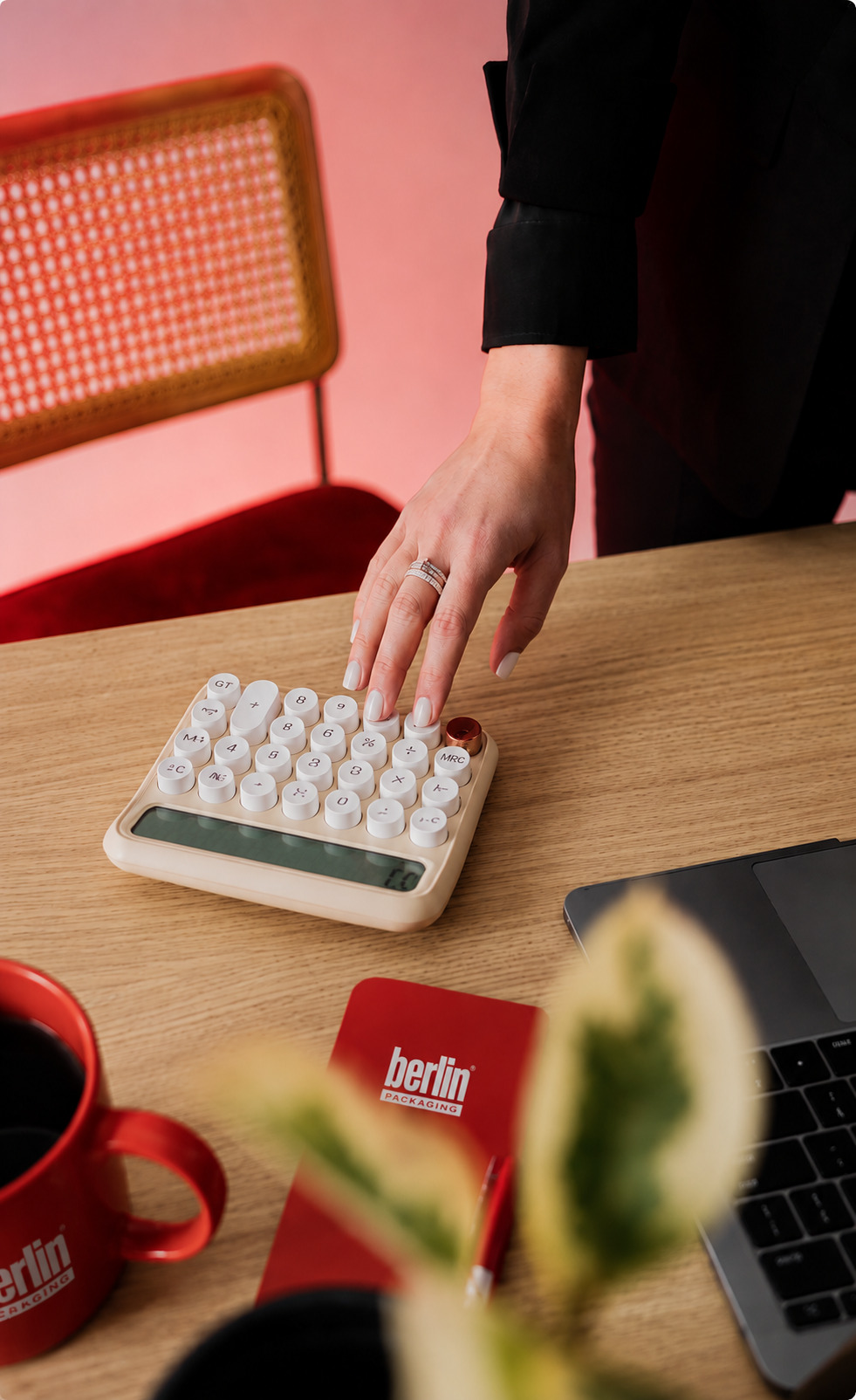 A hand using a keyboard beside a red Berlin Packaging mug on a wooden desk