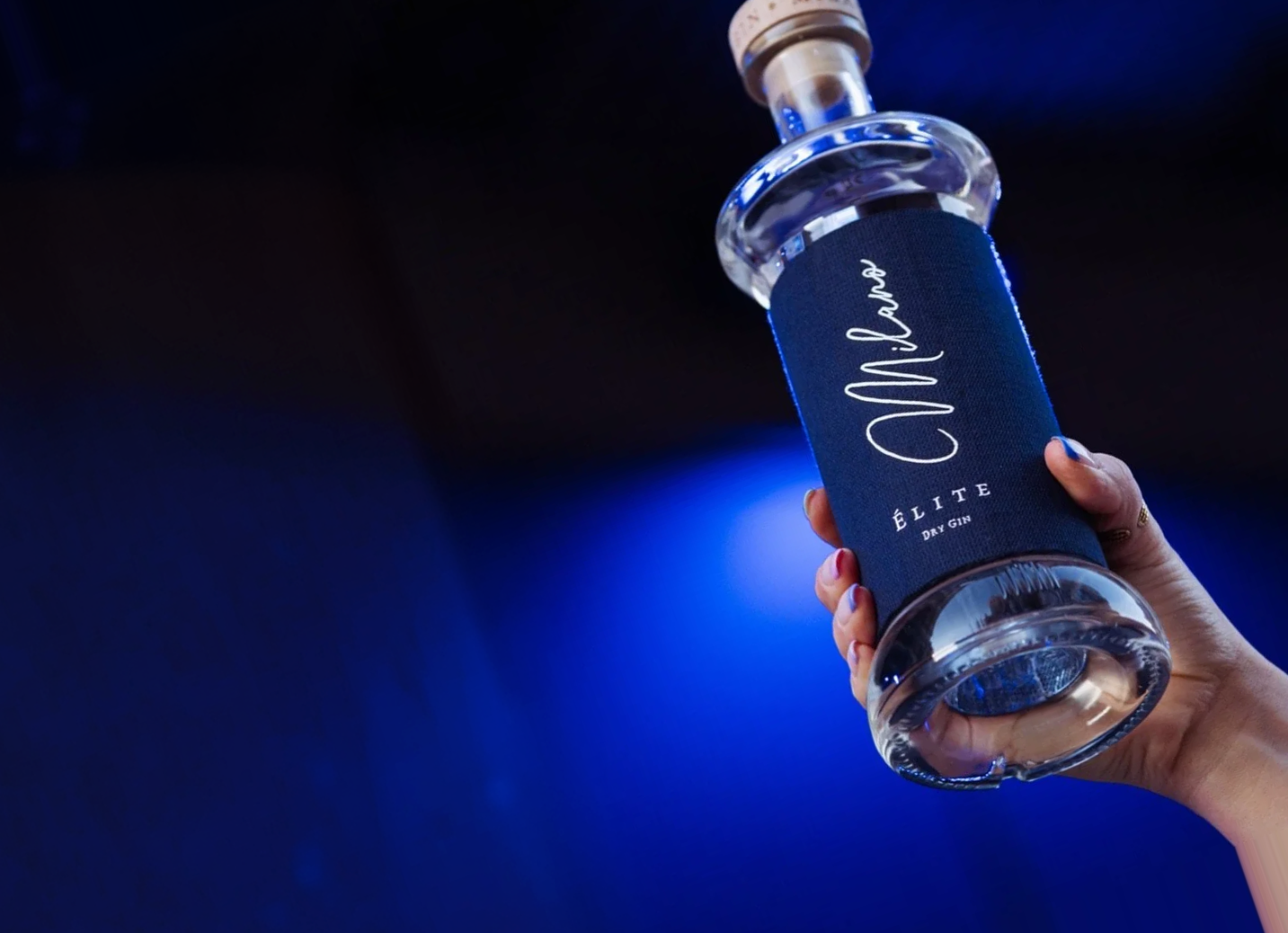 Hand holding a blue Milano Elite dry gin bottle