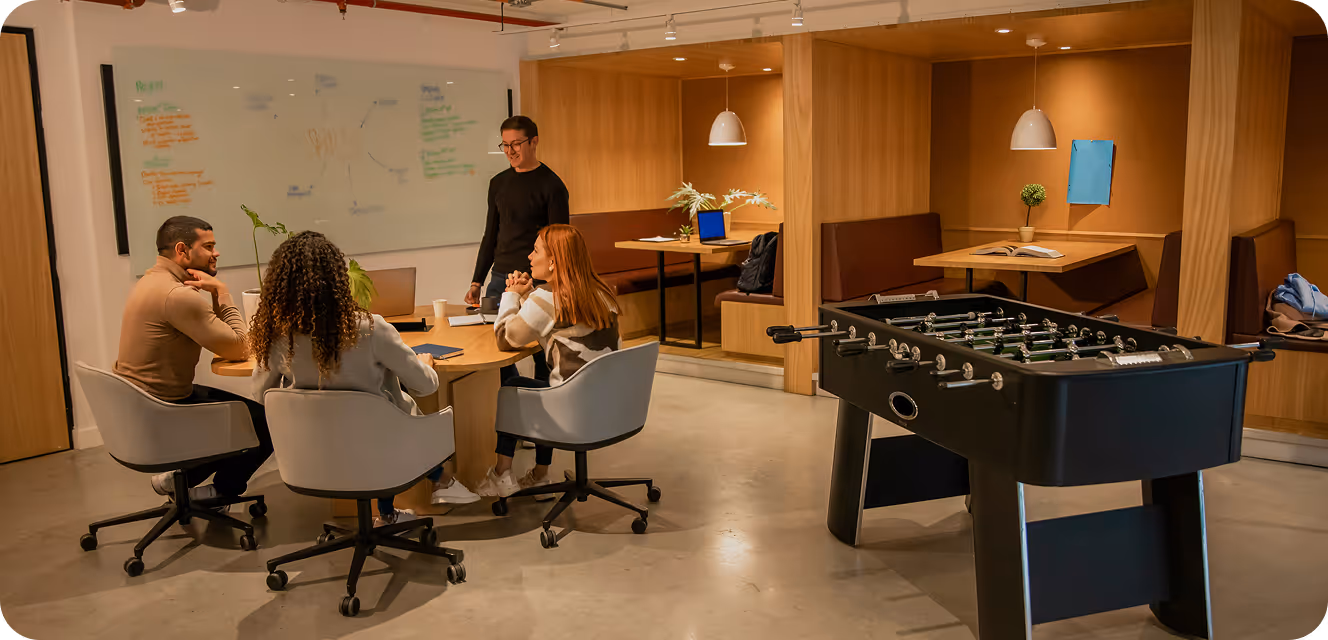 Quatre collègues assis autour d'une table en réunion dans un bureau moderne avec un baby-foot.