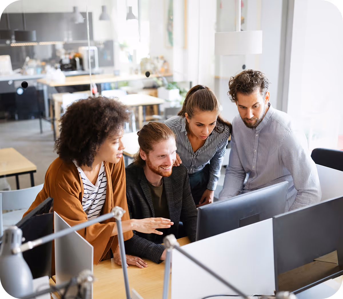 Quatre collègues collaborent autour d'un écran d'ordinateur dans un bureau lumineux et moderne.