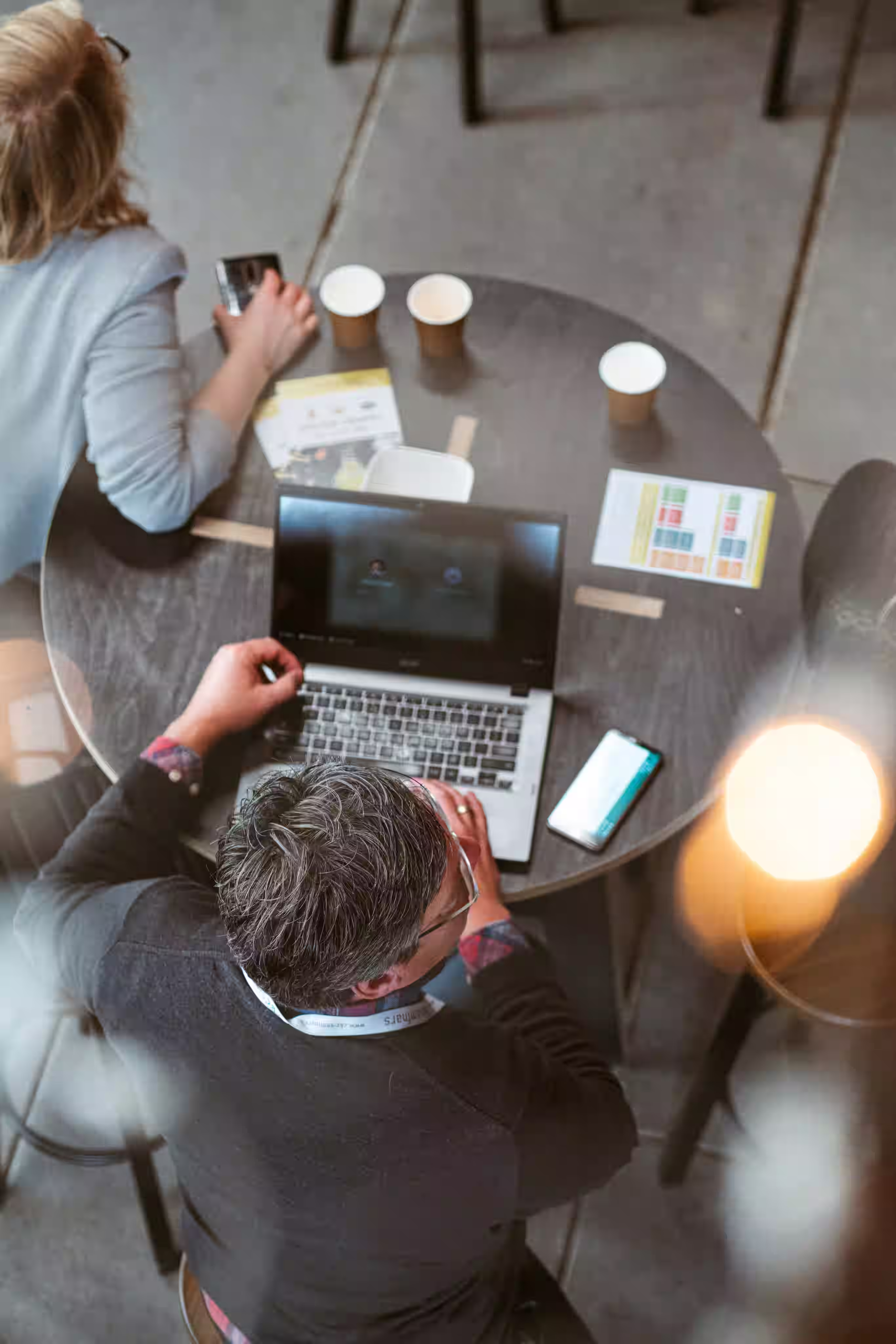 Deux personnes assises à une table ronde, une utilisant un ordinateur portable et l'autre un smartphone.