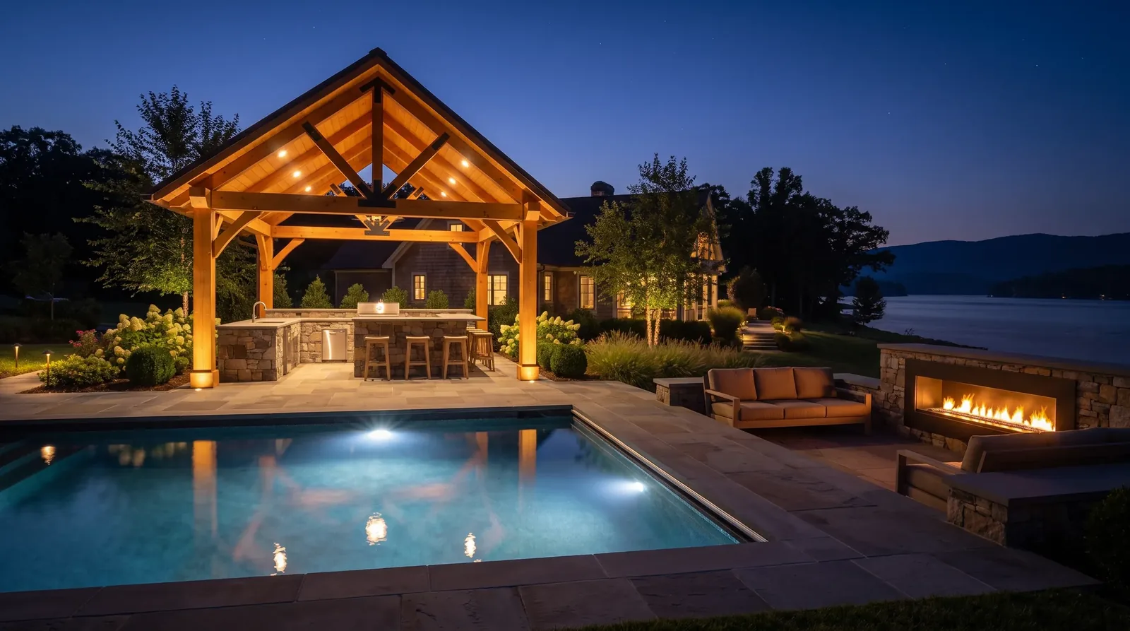 Timber-frame pool pavilion with outdoor kitchen and fireplace at dusk on Smith Mountain Lake VA