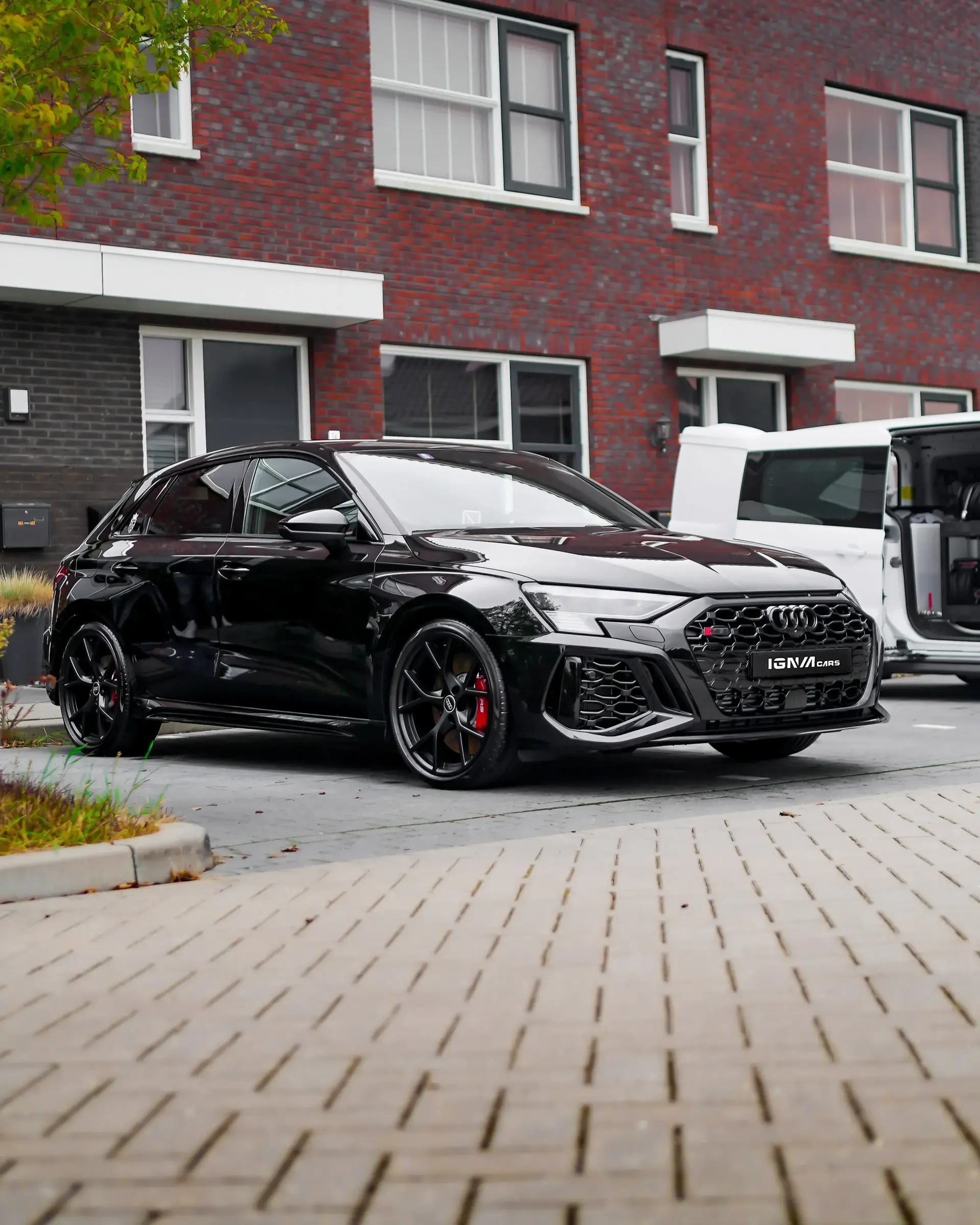 Zwarte Audi S3 sportwagen geparkeerd op een oprit voor een modern bakstenen huis.