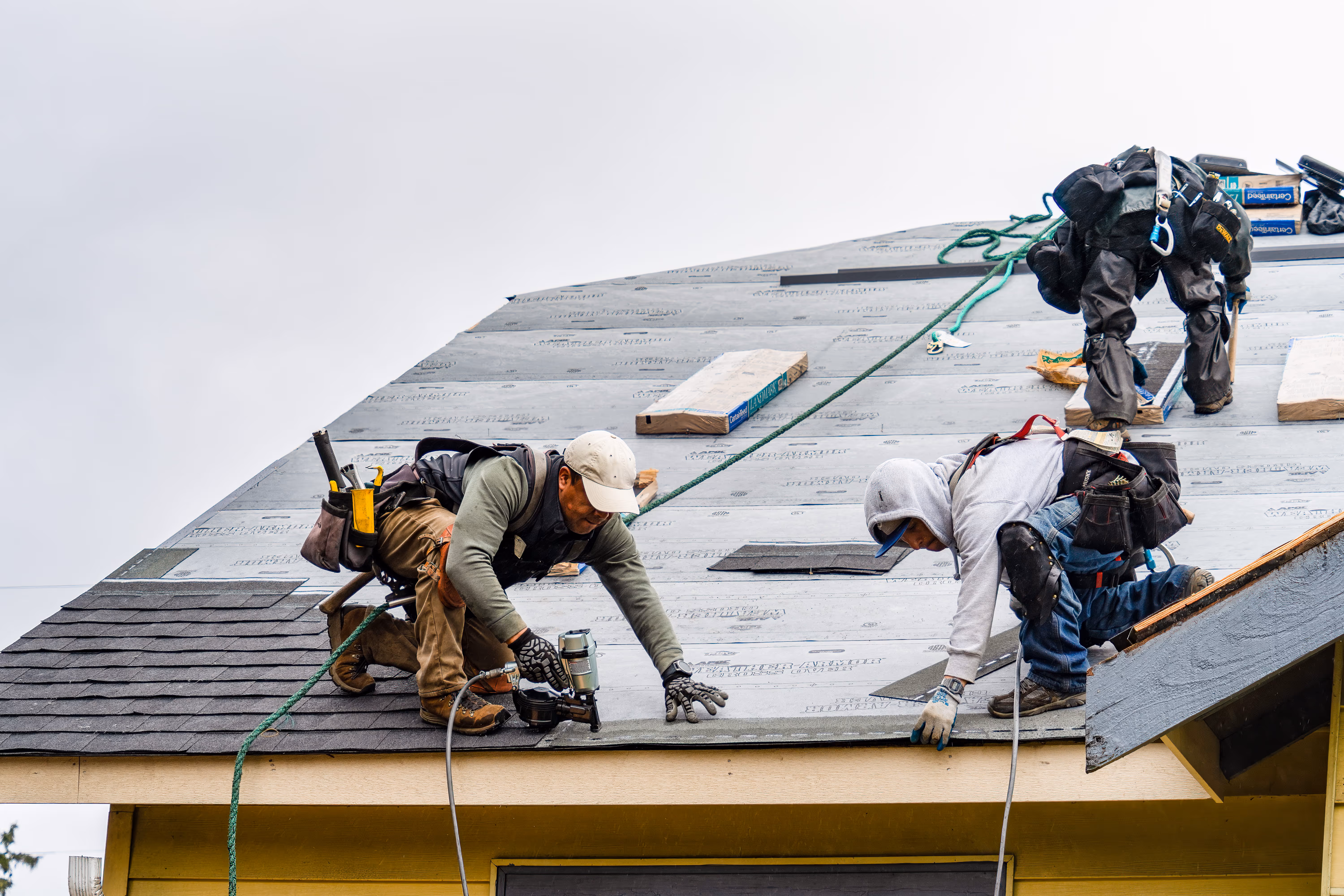 Construction worker using a nail gun to install asphalt roof shingles.