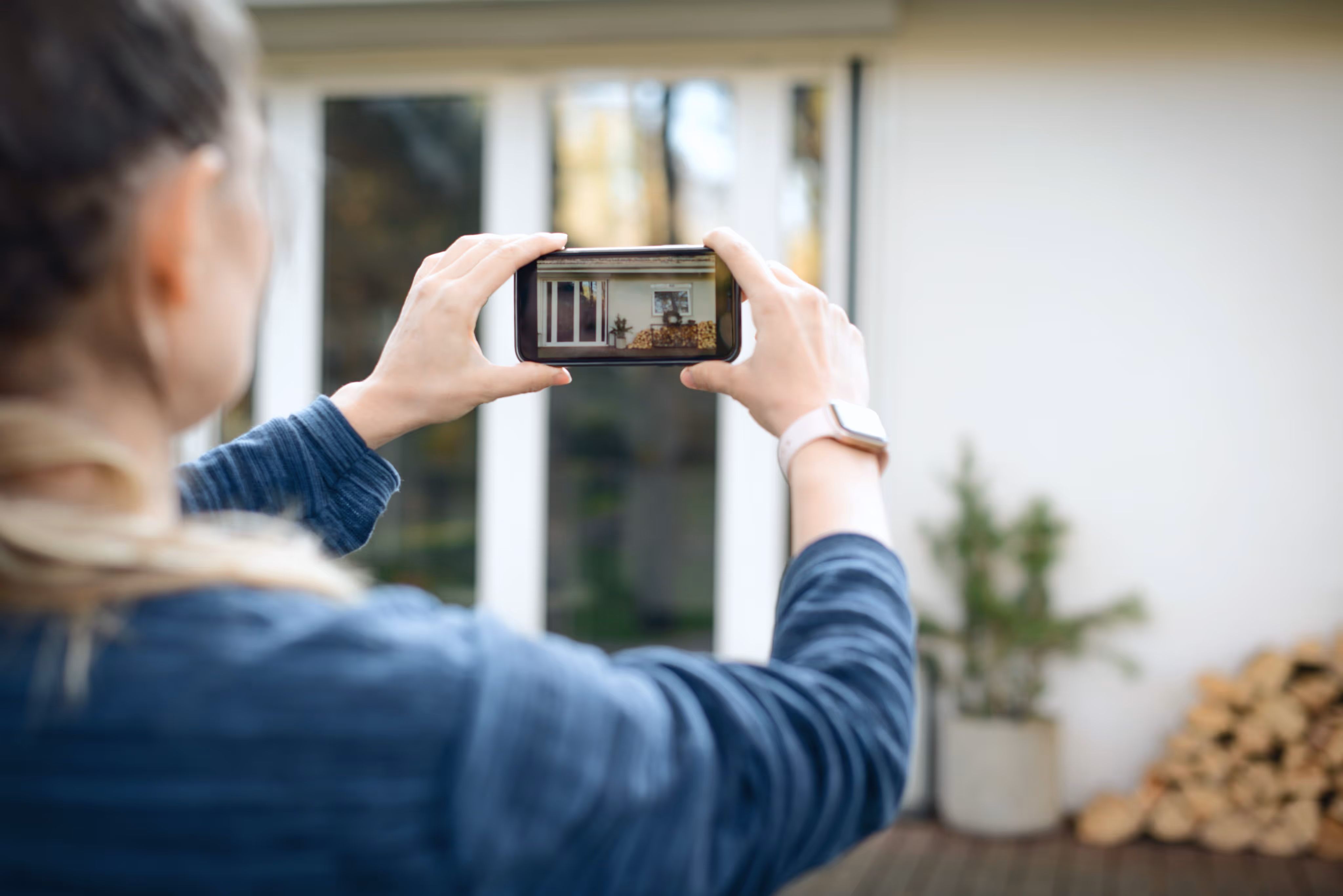 Person holding a smartphone to take a photo of a yellow house with white columns and a porch.
