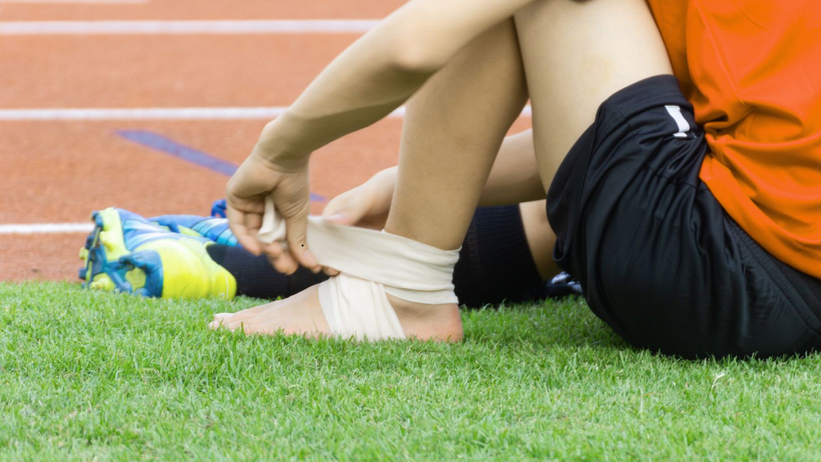 Football player sitting on the pitch with a wrapped ankle, adjusting a bandage during a match, symbolizing injury concerns and confirmed absences affecting team performance.