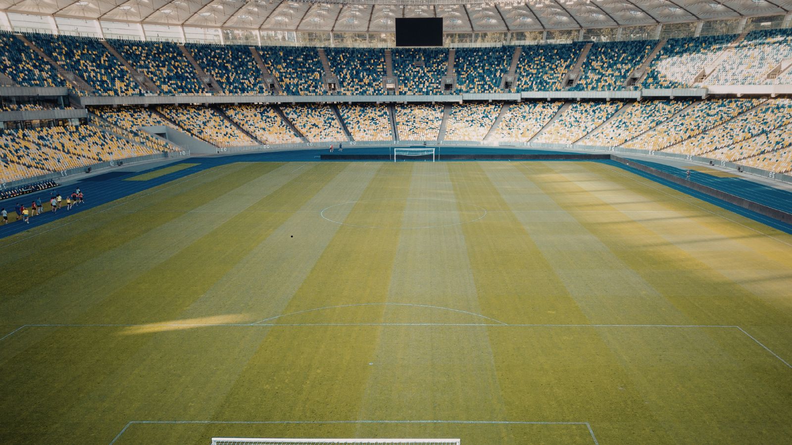 Empty modern football stadium with green pitch, goalposts and colorful seating, captured before kickoff on a clear day.